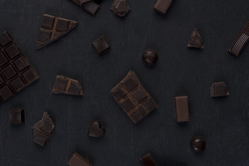 Top view of cracked dark chocolate bar with sweets