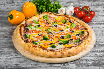 Vegetarian pizza with rosemary and spices on a light wooden background. Italian pizza on a background of green basil and fresh vegetables