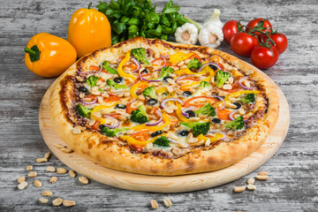 Vegetarian pizza with rosemary and spices on a light wooden background. Italian pizza on a background of green basil and fresh vegetables