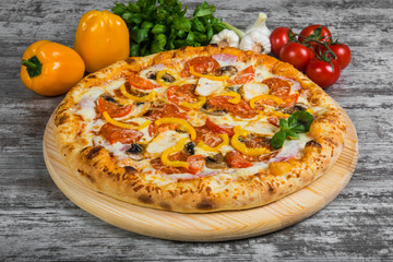 Pizza with sausage, mushrooms, cheese, tomato sauce, rosemary and spices on a light wooden background. Italian pizza on a background of green basil and fresh vegetables