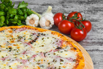 Pizza with ham under cheese, with rosemary and spices on a light wooden background. Italian pizza on a background of green basil and fresh vegetables