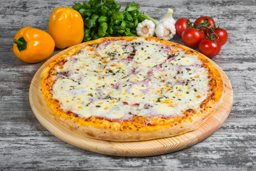 Pizza with ham under cheese, with rosemary and spices on a light wooden background. Italian pizza on a background of green basil and fresh vegetables