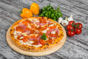 Pizza with sausage, chicken, bacon, ham, with rosemary and spices on a light wooden background. Italian pizza on a background of green basil and fresh vegetables