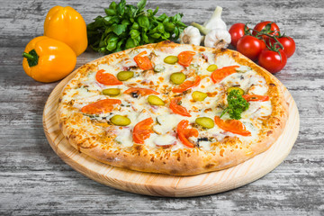 Pizza meat with cheese and cucumber, with rosemary and spices on a light wooden background. Italian pizza on a background of green basil and fresh vegetables