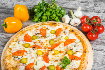 Pizza meat with cheese and cucumber, with rosemary and spices on a light wooden background. Italian pizza on a background of green basil and fresh vegetables