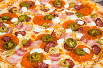 Pizza with smoked meat, with rosemary and spices on a light wooden background. Italian pizza on a background of green basil and fresh vegetables