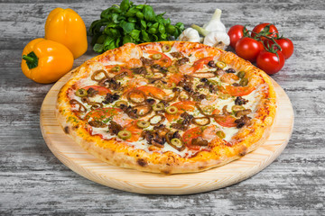 Pizza with seafood, with rosemary and spices on a light wooden background. Italian pizza on a background of green basil and fresh vegetables