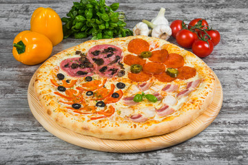 Pizza in four parts, with rosemary and spices on a light wooden background. Italian pizza on a background of green basil and fresh vegetables