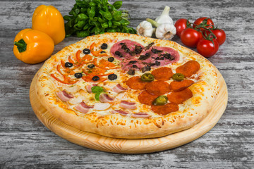 Pizza in four parts, with rosemary and spices on a light wooden background. Italian pizza on a background of green basil and fresh vegetables