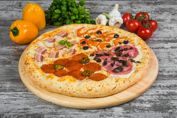 Pizza in four parts, with rosemary and spices on a light wooden background. Italian pizza on a background of green basil and fresh vegetables