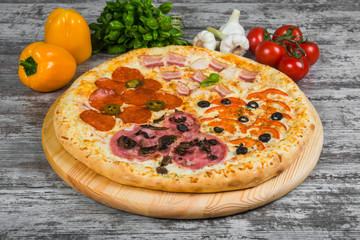 Pizza in four parts, with rosemary and spices on a light wooden background. Italian pizza on a background of green basil and fresh vegetables