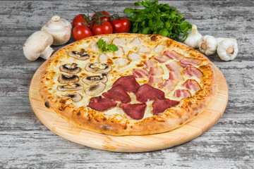 Pizza in four parts, with rosemary and spices on a light wooden background. Italian pizza on a background of green basil and fresh vegetables