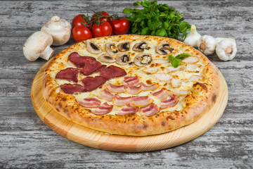 Pizza in four parts, with rosemary and spices on a light wooden background. Italian pizza on a background of green basil and fresh vegetables
