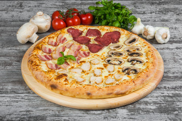 Pizza in four parts, with rosemary and spices on a light wooden background. Italian pizza on a background of green basil and fresh vegetables