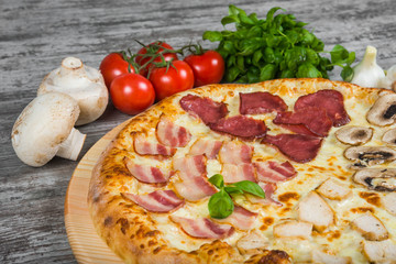 Pizza in four parts, with rosemary and spices on a light wooden background. Italian pizza on a background of green basil and fresh vegetables