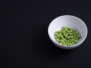 Fresh green podded peas in white bowl isolated on black background