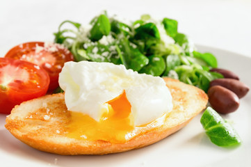 Fototapeta na wymiar poached egg cut open on pan fried white bread, tomato halves, and corn salad with olive oil lemon juice dressing seasoned with parmesan