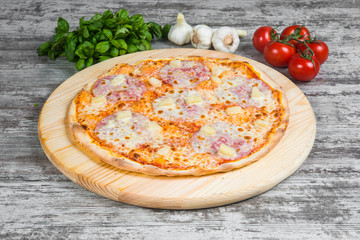 Thin pizza with ham, cheese and pineapple, rosemary and spices on a light wooden background. Italian pizza on a background of green basil and fresh vegetables