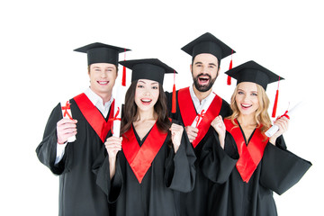 Happy young students in academic caps holding diplomas and smiling at camera