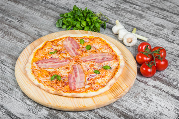 Thin garlic pizza with bacon, tomatoes and onions. Italian pizza on a background of green basil and fresh vegetables