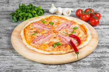 Thin garlic pizza with bacon, tomatoes and onions. Italian pizza on a background of green basil and fresh vegetables