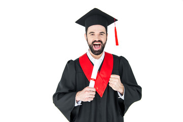 Excited young man in graduation hat holding diploma and triumphing on white