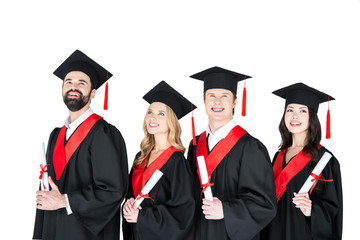 Happy students in graduation gowns and mortarboards holding diplomas on white