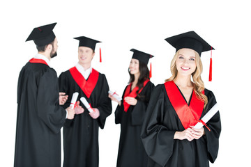 Happy young woman in mortarboard holding diploma and friends standing behind