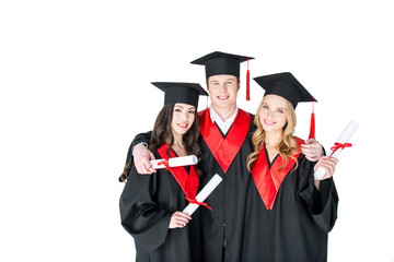 Happy students in academic caps standing embracing with diplomas and looking at camera
