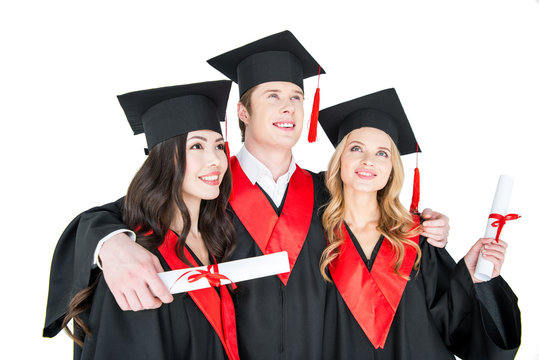 Happy students in academic caps standing embracing with diplomas
