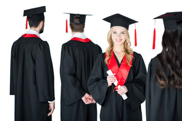 attractive student in graduation cap with diploma, with friends behind isolated on white