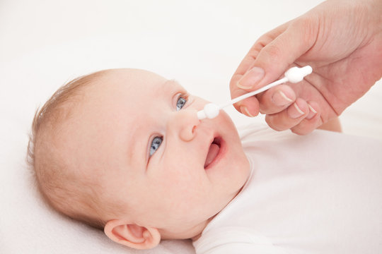 mother cleans nose of a newborn baby whith a cotton bud