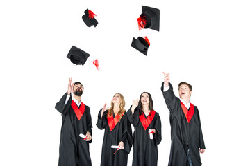 happy young students with diplomas throwing graduation caps isolated on white