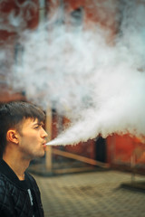Vape. A handsome young white guy blows steam from an electronic cigarette in a vintage old red yard. Vaping.