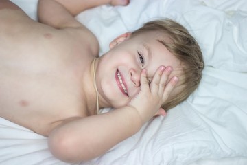 Portrait of a cute little happy boy. Babe fools around in bed.