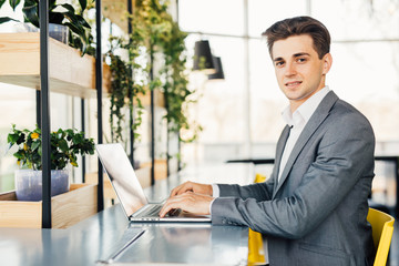Side view of business man sitting by the table with laptop computer and looking at camera.