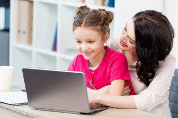 Beautiful happy mother and daughter using laptop at workplace
