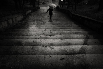Person silhouette with an umbrella is descending the stairs under a heavy rain fall