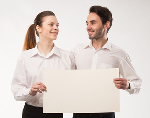 Young happy couple showing presentation pointing on placard over gray background