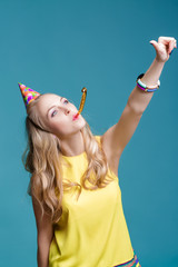 Obraz premium portrait of funny blond woman in birthday hat and yellow shirt on blue background. Celebration and party.