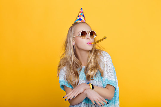 Portrait Of Funny Blond Woman In Birthday Hat And Blue Shirt On Yellow Background. Celebration And Party.