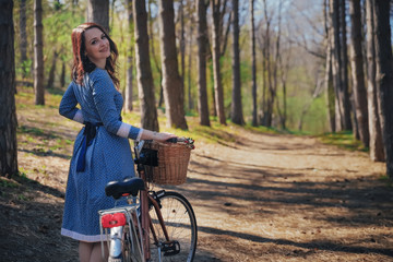 Beautiful young smiling woman with short dark hair and hat standing near bicycle with basket of huge bouquet of chamomiles.Summer girl enjoying the nature outdoor.Green background.
