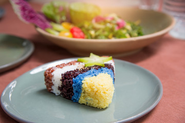 Rice turnovers (brown , white, purple, blue, yellow) on table with food blurred background.