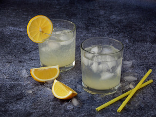 glasses of cold homemade lemonade with lemon slices, ice cubes and straws on dark background. Copy space