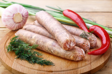 Several raw sausages from pork with beef for grilling lie on a wooden board, close-up. Red chili pepper, green onion, dill.