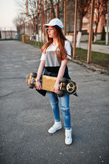Fototapeta na wymiar Young teenage urban girl with skateboard, wear on glasses, cap and ripped jeans at the yard sports ground.