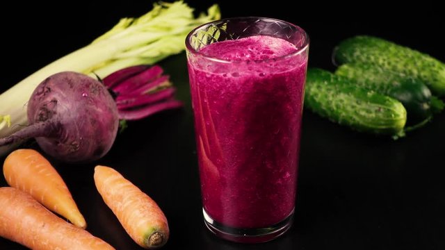 Juice, smoothies from fresh vegetables, carrots, celery, beets and cucumbers fills a glass, on a black table. High speed