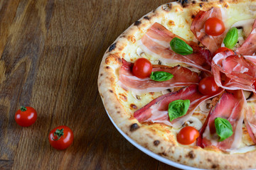 Neapolitan pizza with cream sauce, bacon, mozzarella and cherry tomatoes, served on a wooden table for a dinner in italian restaurant. Italy food. Pizza from wooden oven. Close up. Macro.