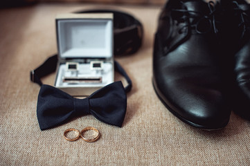 Close up of modern man accessories. wedding rings, black bowtie, leather shoes, belt and cufflinks