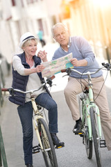 Senior couple riding bikes and reading map in tourist area